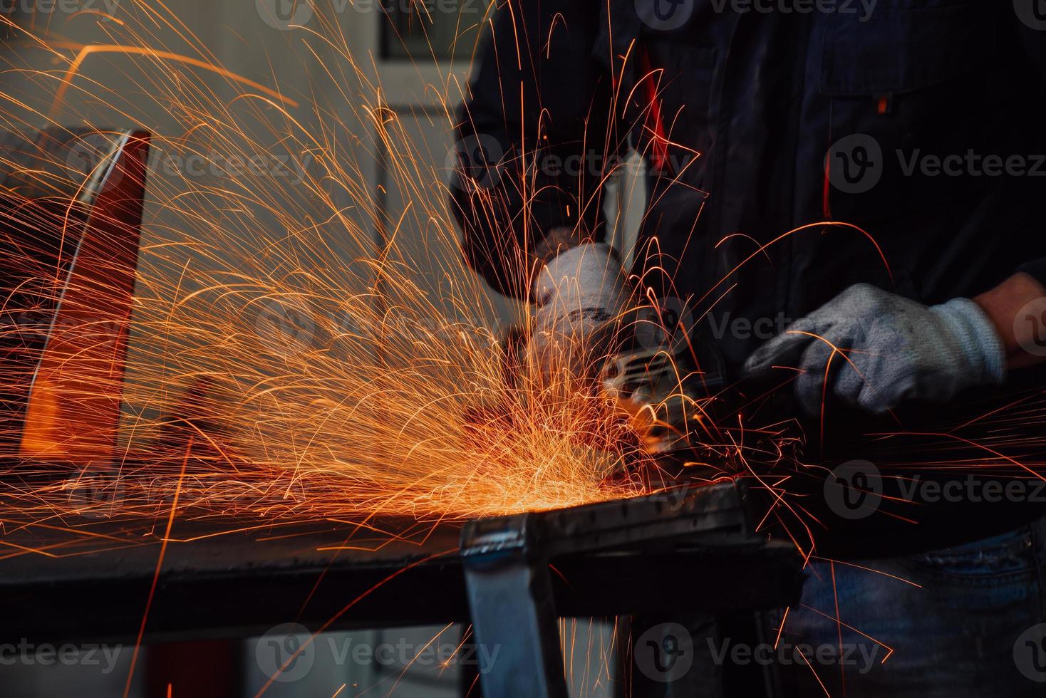 schwerindustrie-fabrikinnenraum mit industriearbeiter, der winkelschleifer verwendet und ein metallrohr schneidet. Auftragnehmer in der Herstellung von Metallstrukturen für Sicherheitsuniformen und Schutzhelme. foto