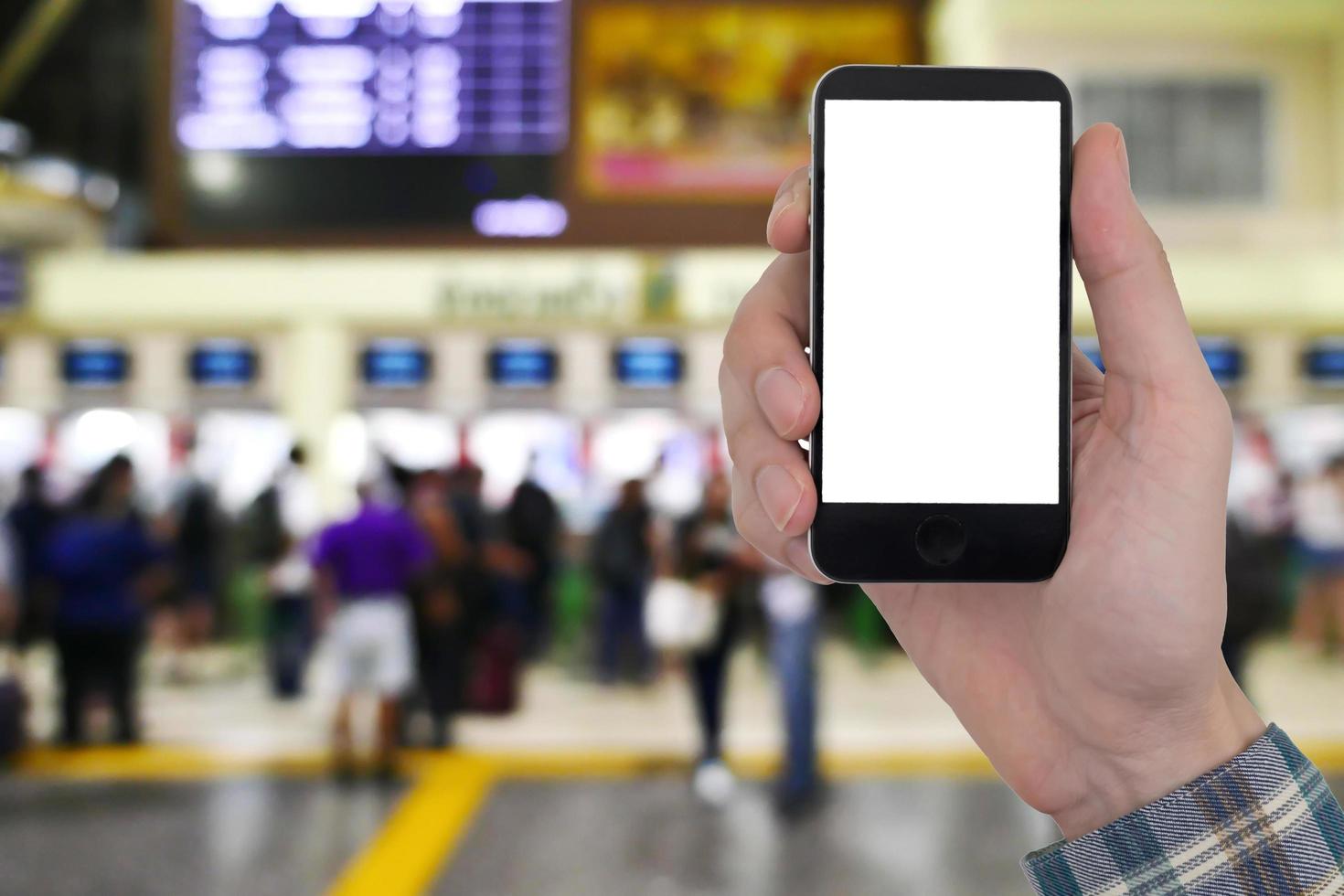Männliche Hände, die ein Smartphone mit einem leeren weißen Bildschirm auf einem verschwommenen Bild von Menschen halten, kaufen ein Ticket am Schalterhintergrund. foto
