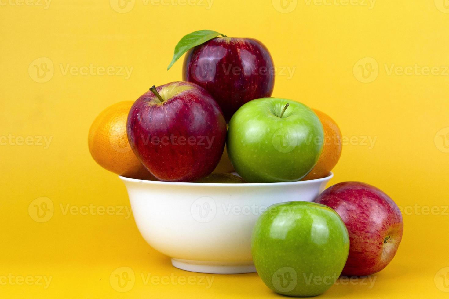 frische erdige früchte, grüne äpfel, roter apfel, orangen isoliert auf gelbem hintergrund. gesunde früchte in einer weißen schüssel auf gelbem hintergrund. Wird für Kochkonzeptanzeigen verwendet foto