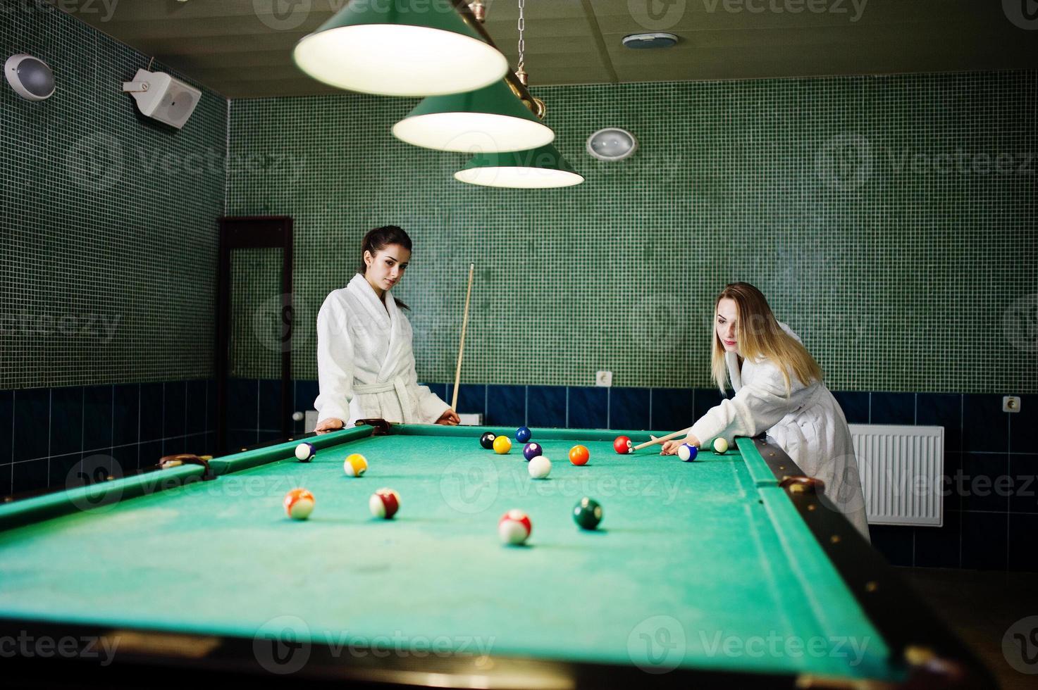 Zwei sexy Mädchen im weißen Bademantel spielen Billard. foto