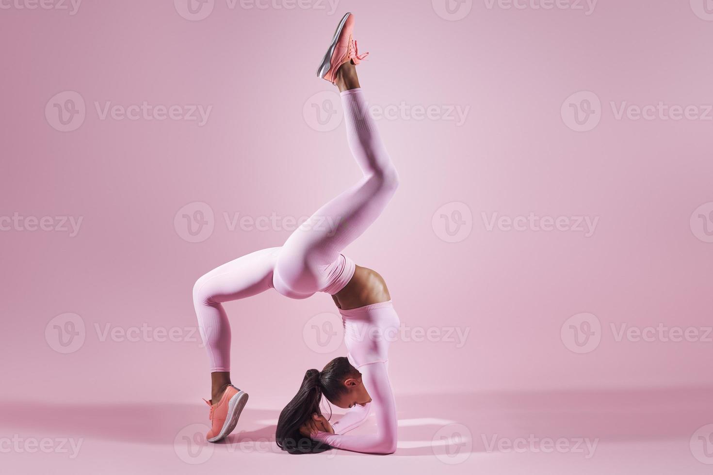 Schöne junge Frau in Sportkleidung, die Dehnübungen vor rosafarbenem Hintergrund macht foto