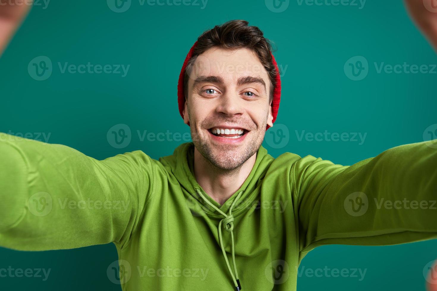 glücklicher junger Mann, der durch einen Fingerrahmen schaut, während er vor grünem Hintergrund steht foto