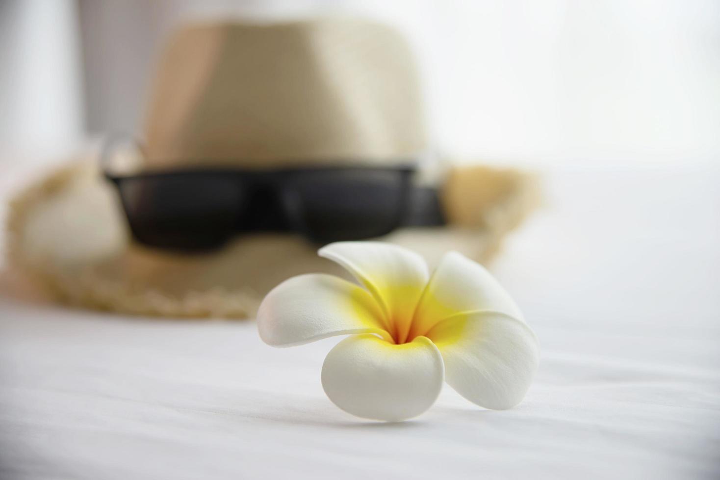 touristische sachen hut sonnenbrille und plumeria blume im weißen bettzimmer - glücklicher entspannungsurlaub urlaub und hotelkonzept foto