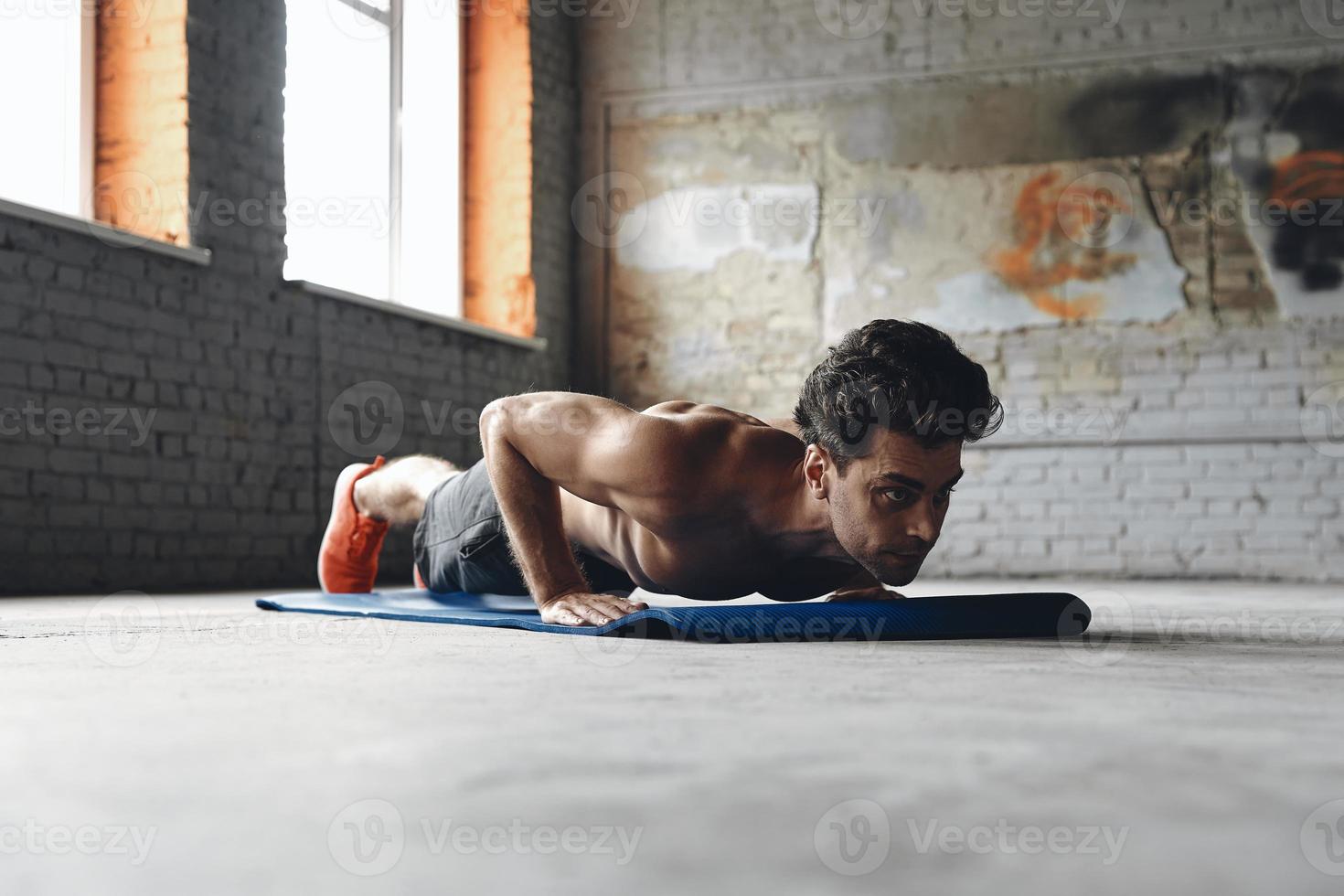 Selbstbewusster junger Mann, der Liegestützübungen im Fitnessstudio macht foto