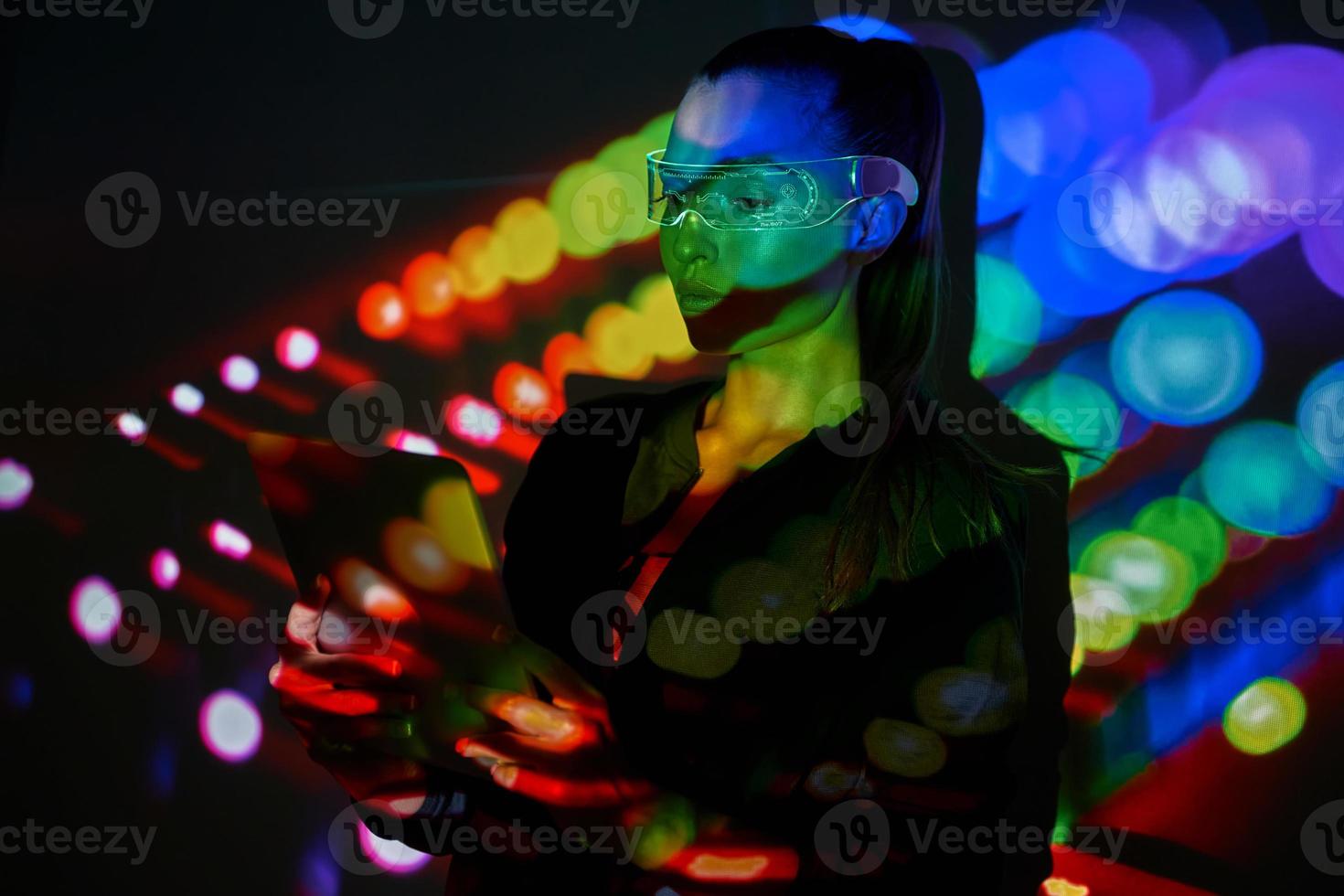 Selbstbewusste Frau in futuristischer Brille mit digitalem Tablet vor buntem Hintergrund foto