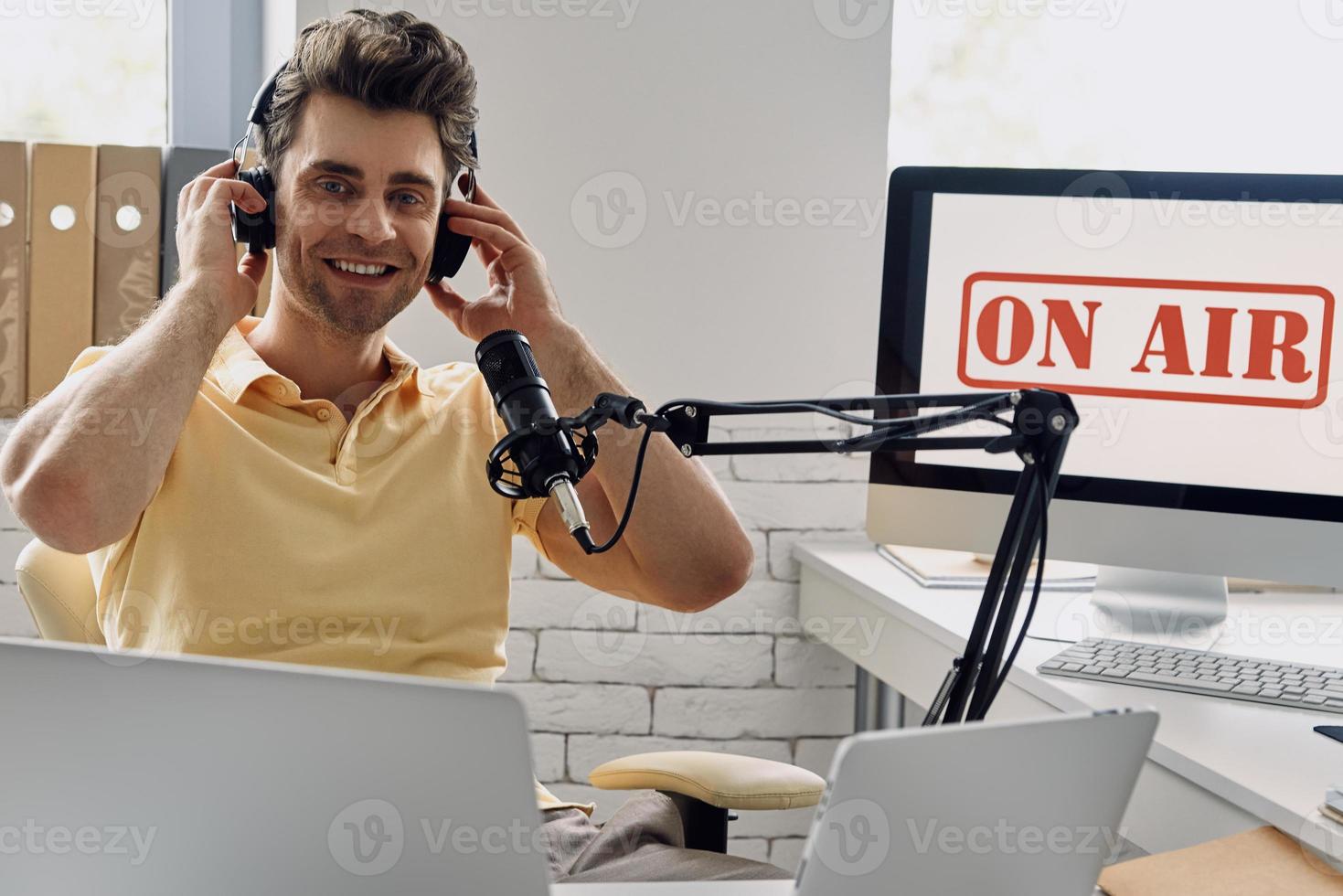 gutaussehender junger mann mit kopfhörern, der mikrofon verwendet, während er podcast im studio aufnimmt foto