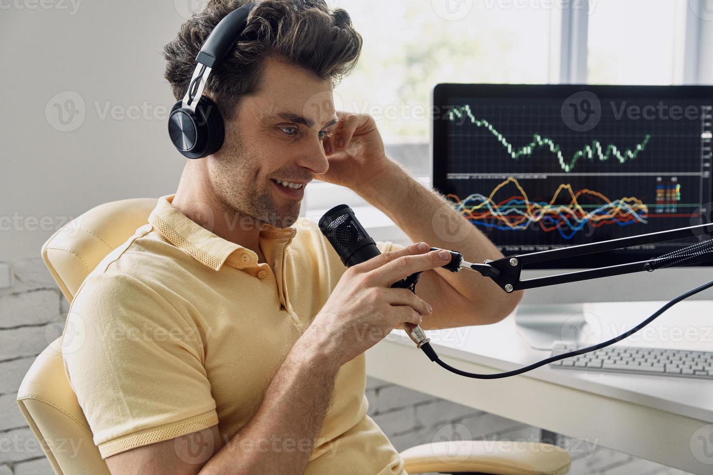 Fröhlicher Mann mit Kopfhörern, der ein Mikrofon verwendet, während er seinen Business-Podcast aufzeichnet foto