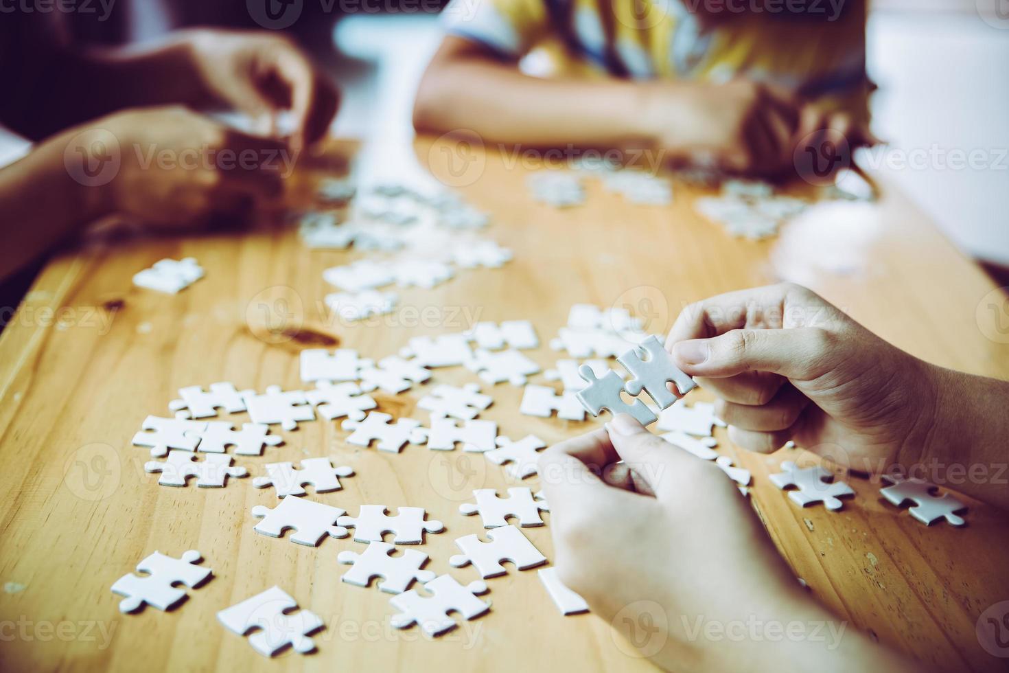Hände einer Person, kleines Kind und Elternteil, die zu Hause zusammen auf einem Holztisch ein Puzzlespiel spielen, Konzept für die Freizeit mit der Familie, Spiel mit der Entwicklung, Bildung und Spaß der Kinder. foto