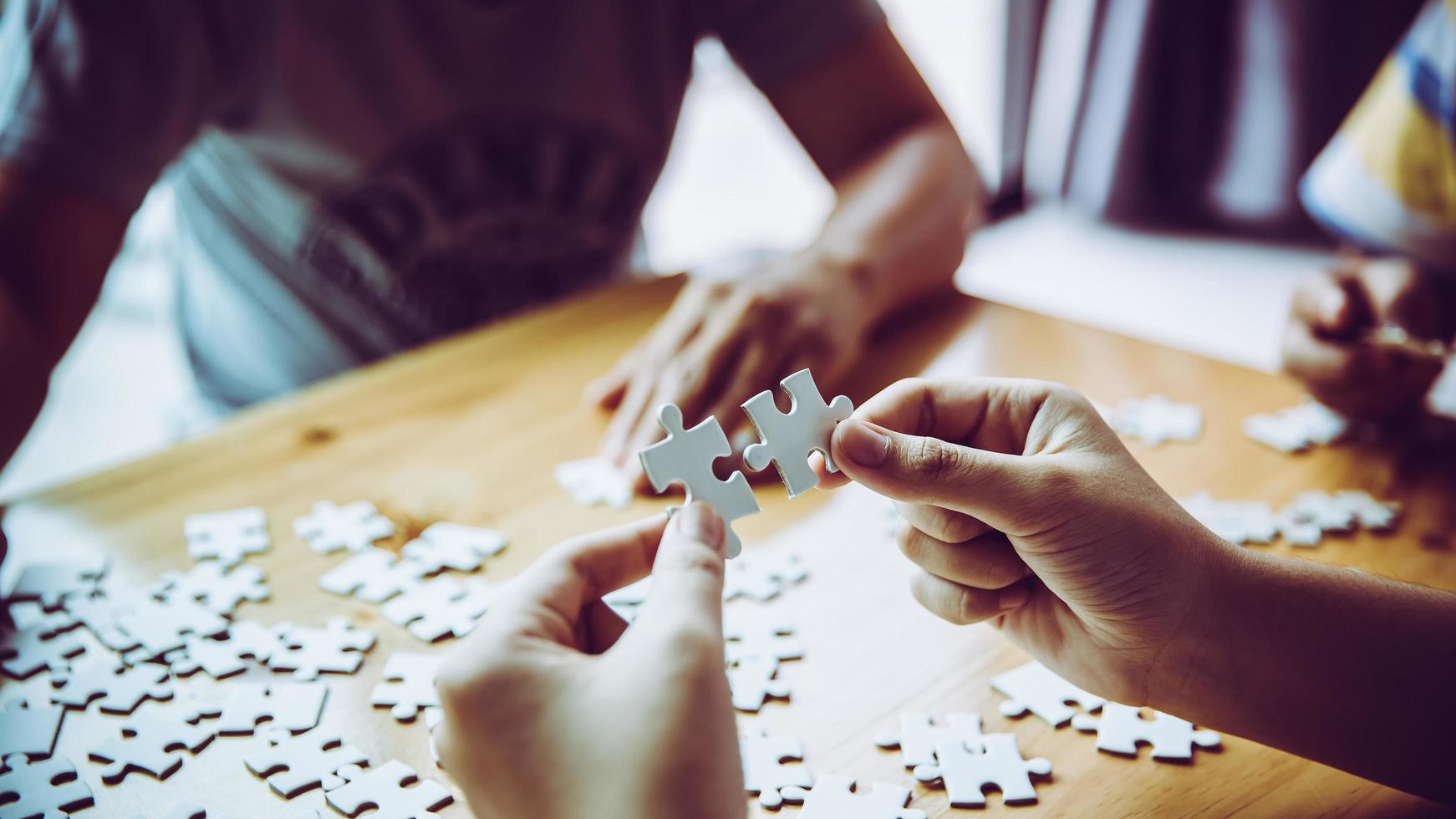 Hände einer Person, kleines Kind und Elternteil, die zu Hause zusammen auf einem Holztisch ein Puzzlespiel spielen, Konzept für die Freizeit mit der Familie, Spiel mit der Entwicklung, Bildung und Spaß der Kinder. foto