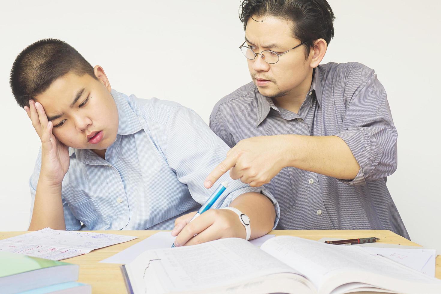 asiatischer vater, der seinem 14-jährigen sohn ernsthaft hausaufgaben beibringt foto