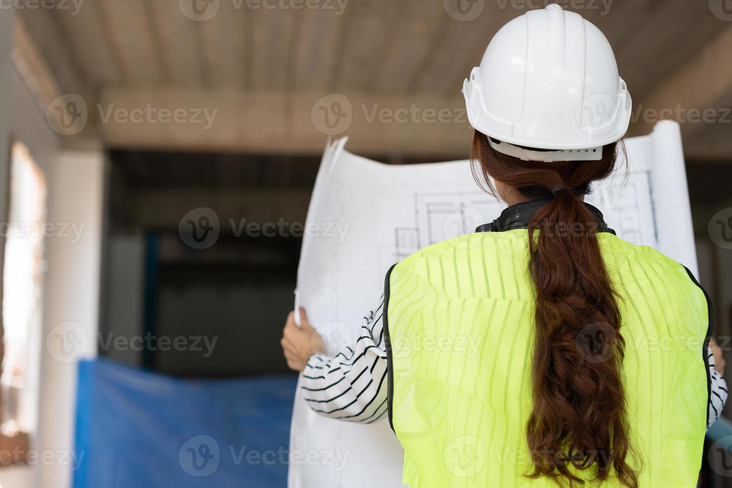 asiatischer ingenieur oder junge architektin setzen aus sicherheitsgründen einen helm auf und sehen sich den bauplan an, um die baustelle einer fabrik auf einer baustelle zu inspizieren. Konzept der intelligenten berufstätigen Frau. foto