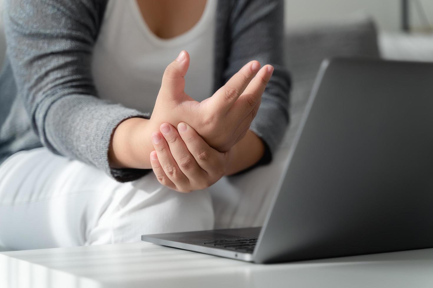 frau, die ihre handschmerzen hält, wenn sie den computer lange benutzt. Office-Syndrom-Konzept. foto