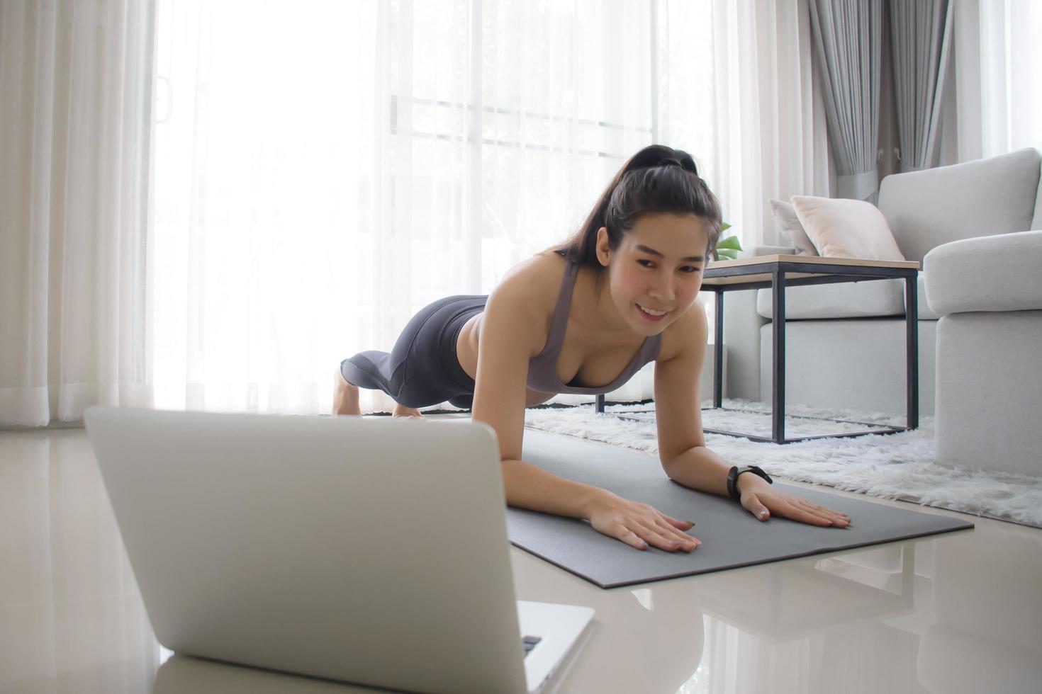 Heimtraining. Sportliche Mädchenübung auf Yogamatte in schwarzer Position Training für Kernkörper und Bauch, während Online-Tutorial über Laptop mit Personal Trainer angesehen wird. foto