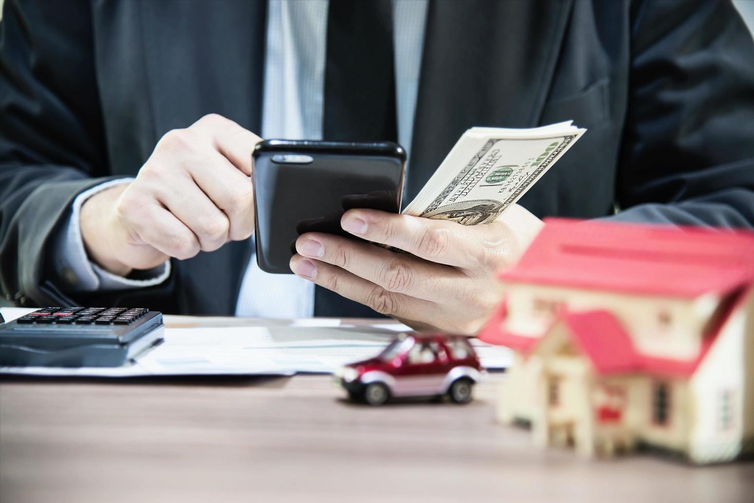 Geschäftsmann, der Gelddollarschein zählt und Haus- und Autokredite berechnet - persönliches Finanzversicherungslebensstil-Immobilienkonzept foto