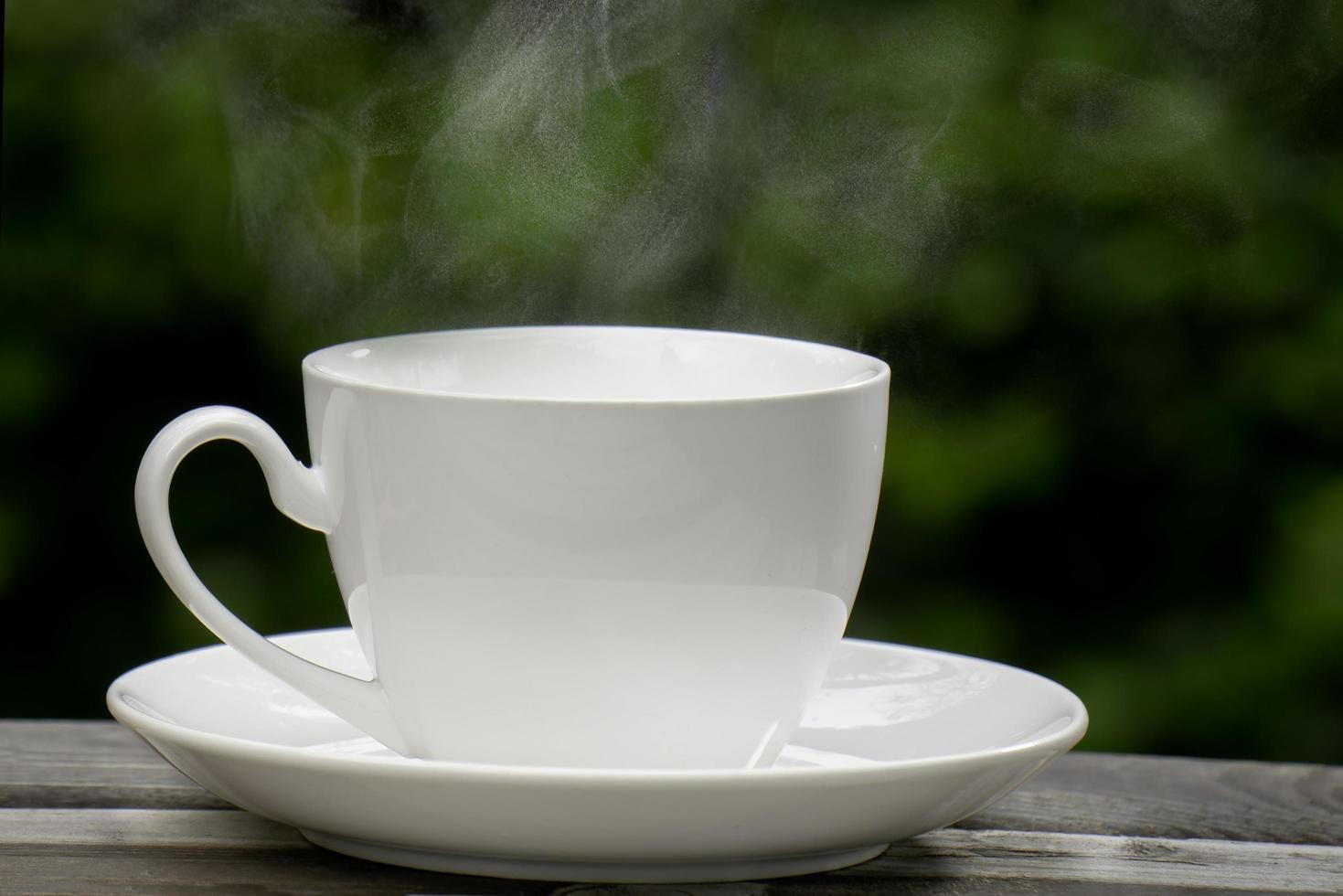 heißes kaffeegetränkkonzept, heiße keramische weiße kaffeetasse mit rauch auf einem alten holztisch in einem natürlichen hintergrund. foto