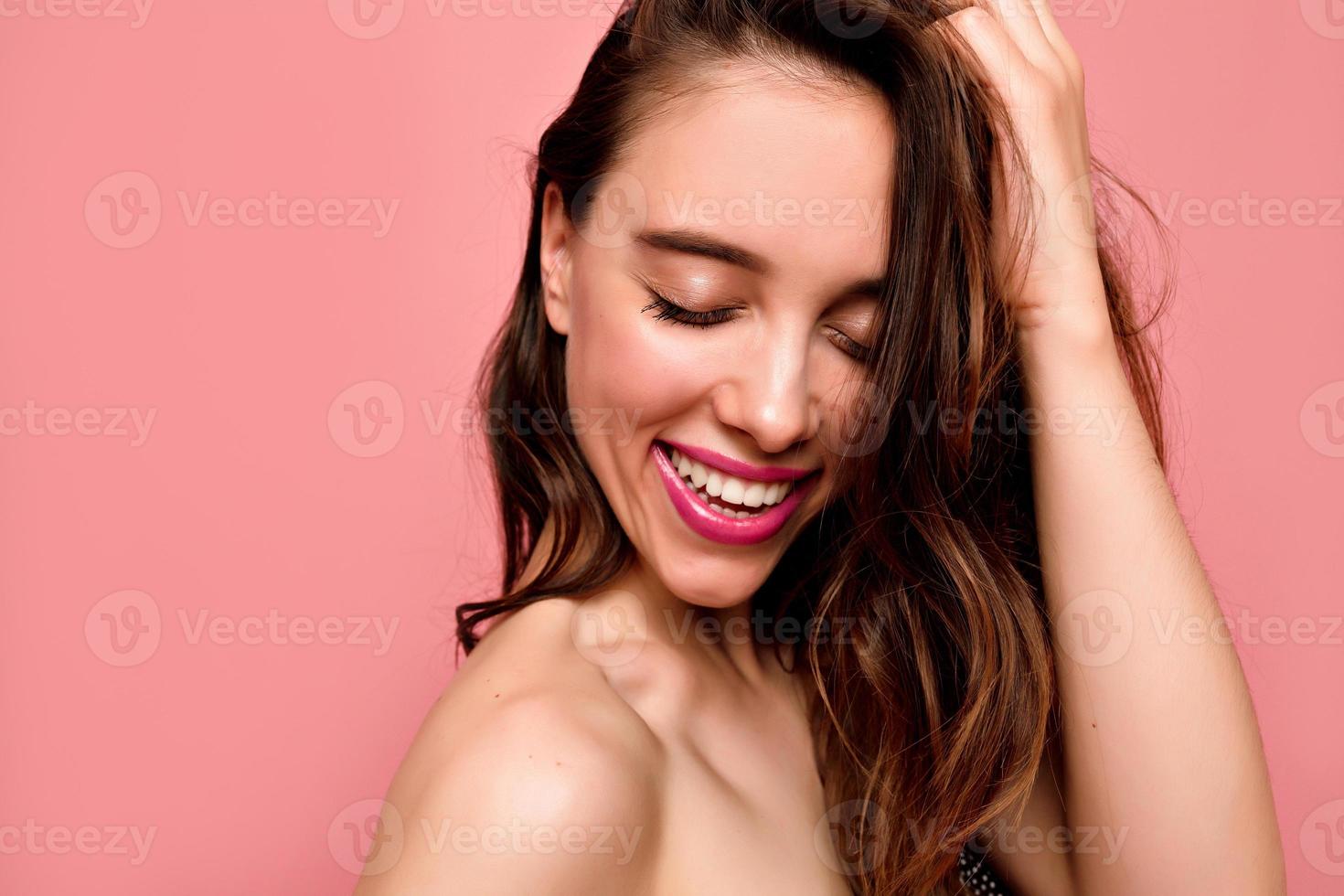 Nahaufnahme Porträt einer schönen jungen lächelnden Frau mit weißen Zähnen und rosa Lippen mit geschlossenen Augen auf rosa Hintergrund foto