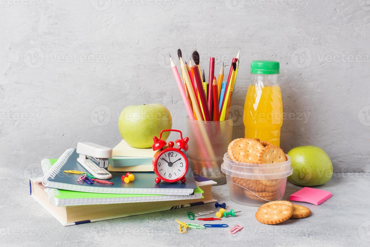 schulbedarf und frühstückscracker, orangensaft und frischer apfel auf dem grauen tisch mit kopierraum. Konzept Schule. foto