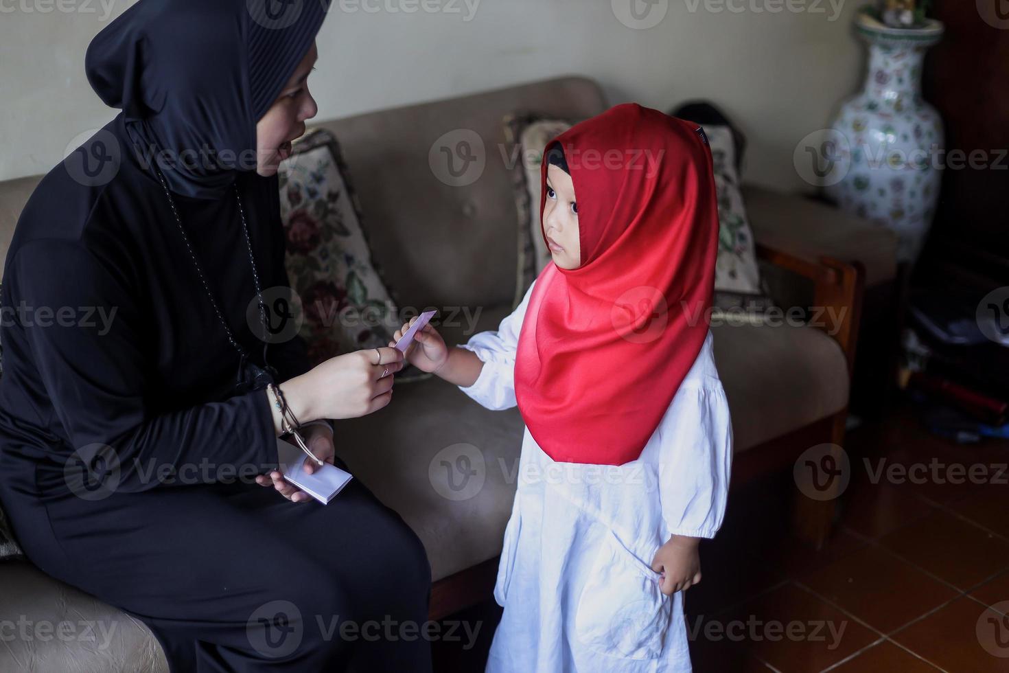 indonesische Volkstradition während der Eid Mubarak-Feier des Verteilens von Geld oder Thr genannt. asiatische muslimische frau gibt süßem jungen der familie während idul fitri geld. foto