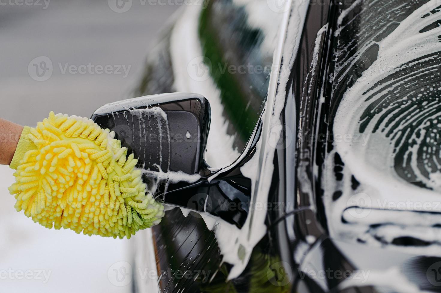 nicht erkennbarer mann wäscht schwarzes auto mit tuch oder lappenhandschuh, verwendet spezialwaschmittel. schmutziges auto reinigen. Geschäftskonzept für Autowäsche. foto