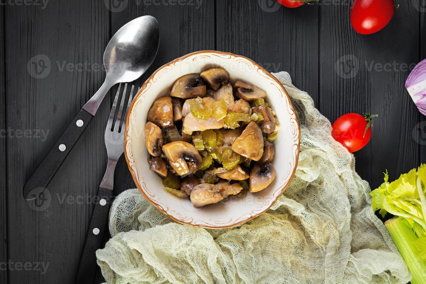 Hähnchenschenkel mit Champignons, Sellerie, Zwiebeln und Paprika geschmort. Hühnchen unter Rühren auf Holzhintergrund braten foto