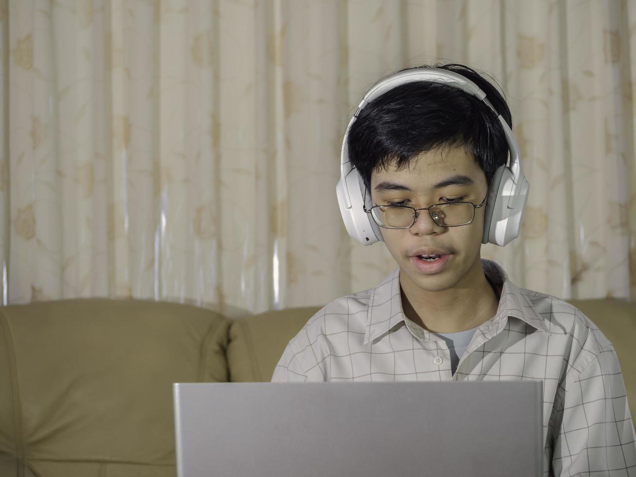 der junge, der kopfhörer trägt, sitzt am tisch mit internet-chat-skype-lehrer, bereitet sich auf die prüfung vor und benutzt laptop-computer für seine hausaufgaben und e-learning für online-bildung. Lernkonzept für Kinder. foto