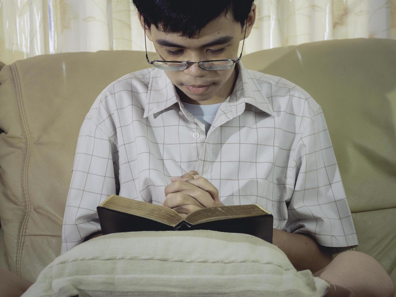 asiatische junge beten um gottsegen für den wunsch, ein besseres leben mit seinen händen auf der bibel in der christlichen kirche zu haben. und beten im Gottesdienstraum. Händchen haltend im Gebet auf der Bibel. foto