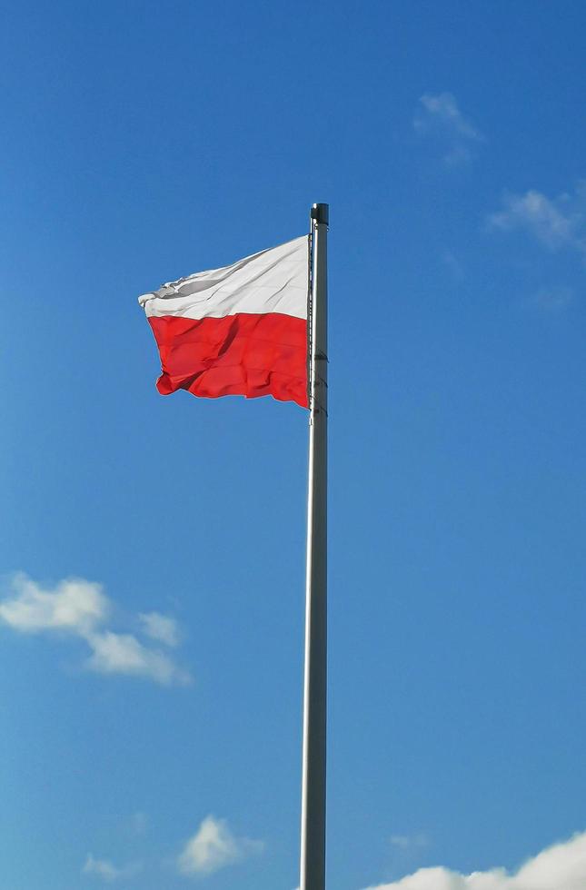 die staatsflagge von polen auf einer stange auf einem hintergrund des blauen himmels im windtag foto