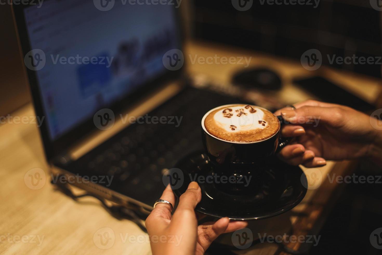 Freiberuflerin, die online am Computer arbeitet, während sie eine Latte-Art-Kaffeetasse hält. konzept der vernetzung und beschäftigung. foto