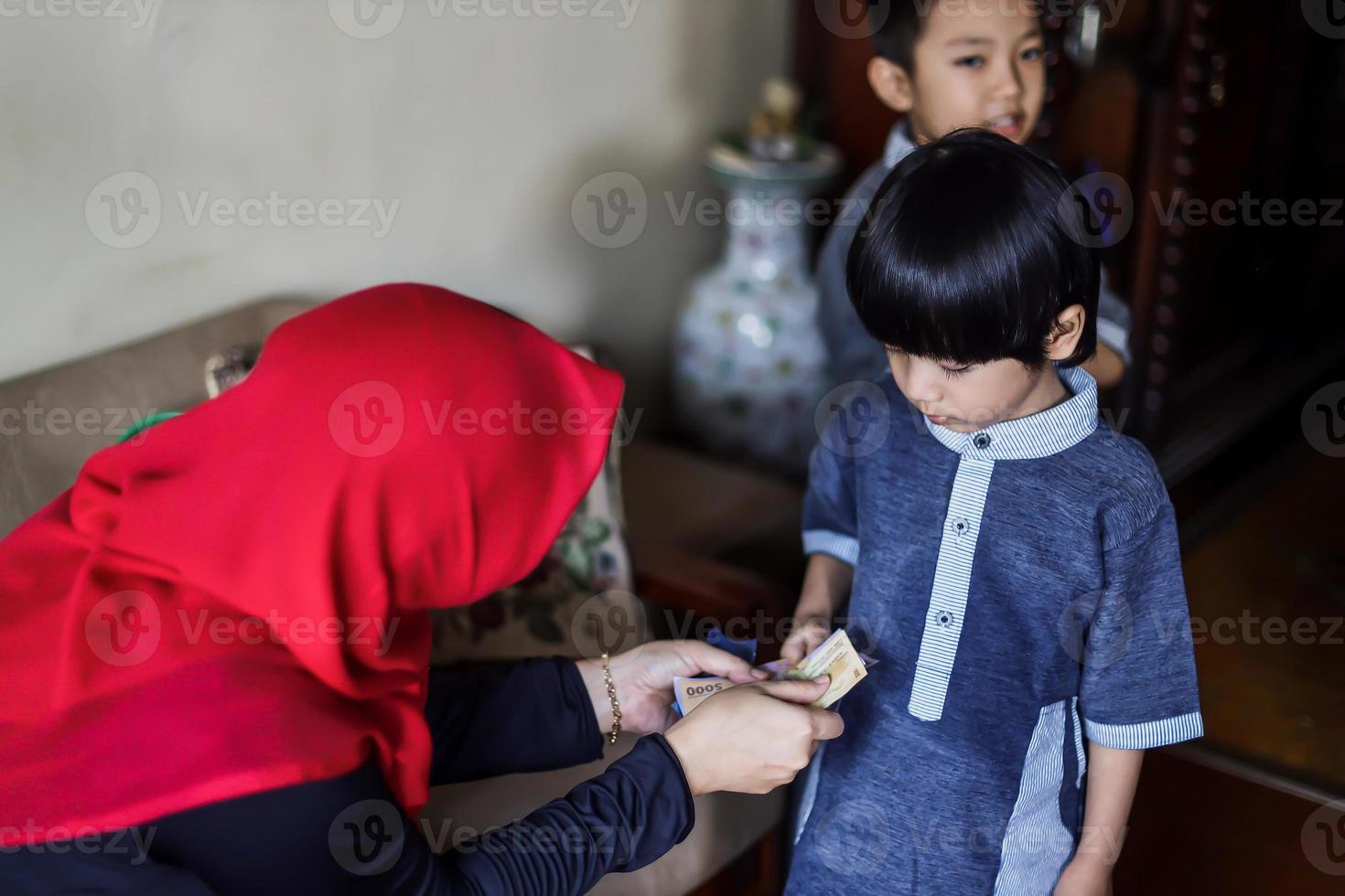 indonesische Volkstradition während der Eid Mubarak-Feier des Verteilens von Geld oder Thr genannt. asiatische muslimische frau gibt süßem jungen der familie während idul fitri geld. foto