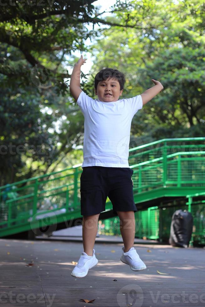 Energischer asiatischer süßer Junge, der im Park im Freien springt und die Hände hochhebt. foto