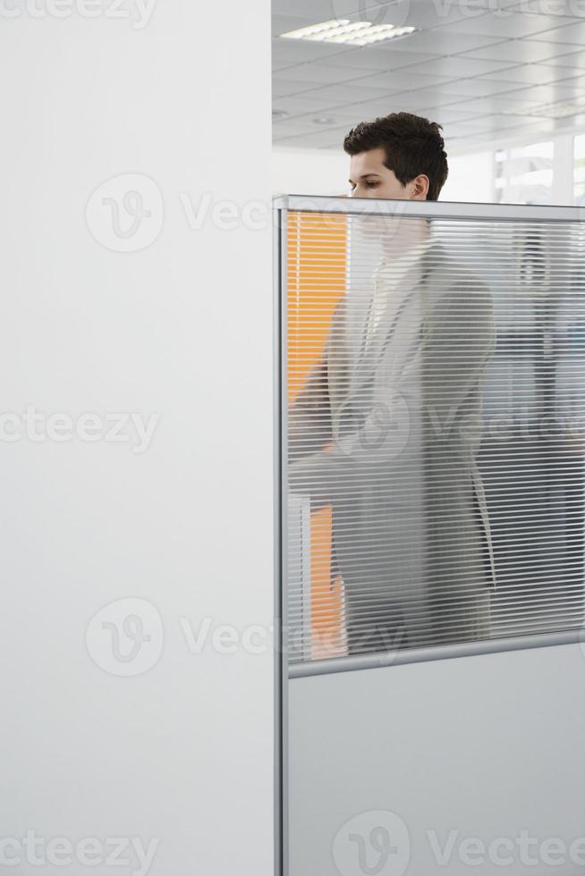 Büroangestellter, der hinter Kabinenwand steht foto