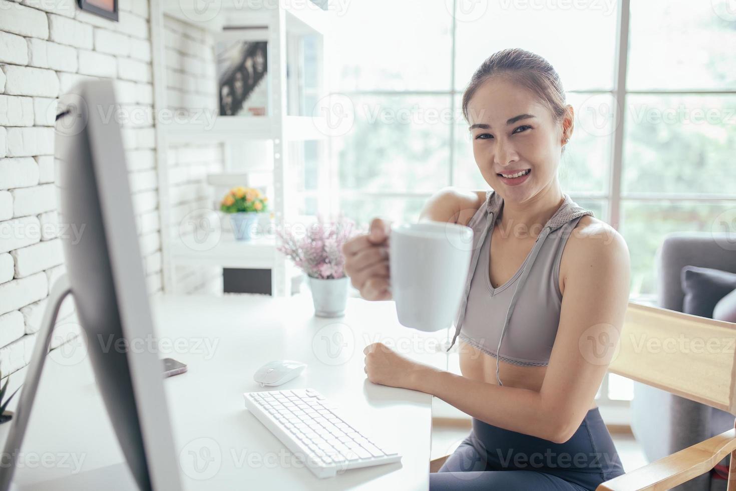 junge asiatische frau, die einen laptop verwendet, der die social-media-anwendung auf der website online mit kaffee zu hause überprüft, fühlt sich entspannt und genießt es, im wohnzimmer zu kommunizieren und zu diskutieren. foto