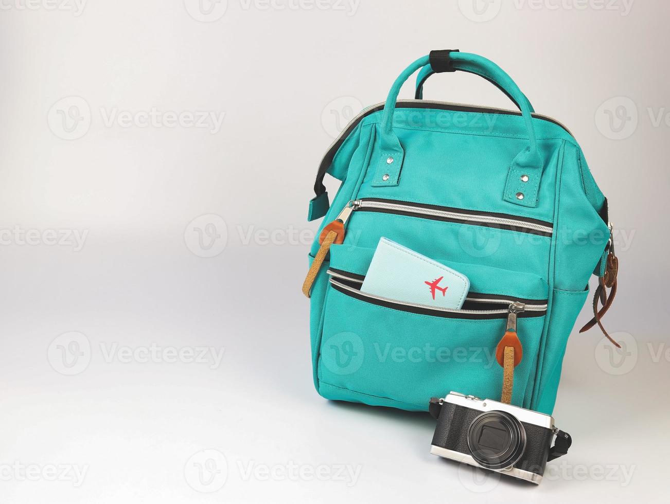 grüner rucksack mit passhülle und kamera auf weißem hintergrund mit kopienraum. reisezubehörkonzept. foto
