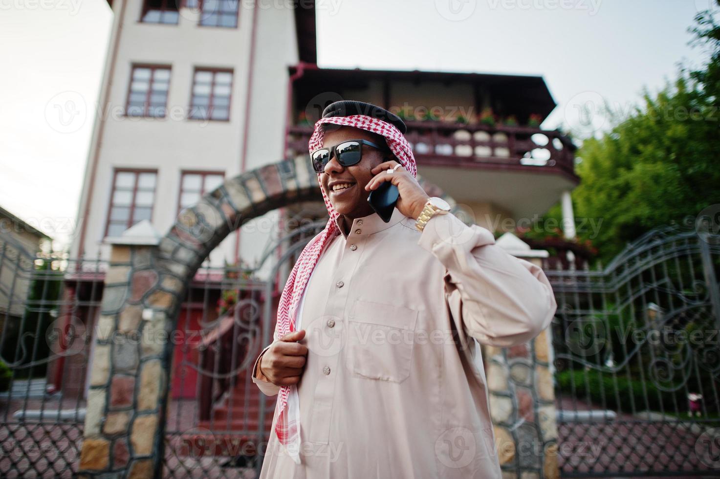 reicher arabischer geschäftsmann aus dem nahen osten mit sonnenbrille posierte auf der straße gegen das herrenhaus und sprach mit dem handy. foto
