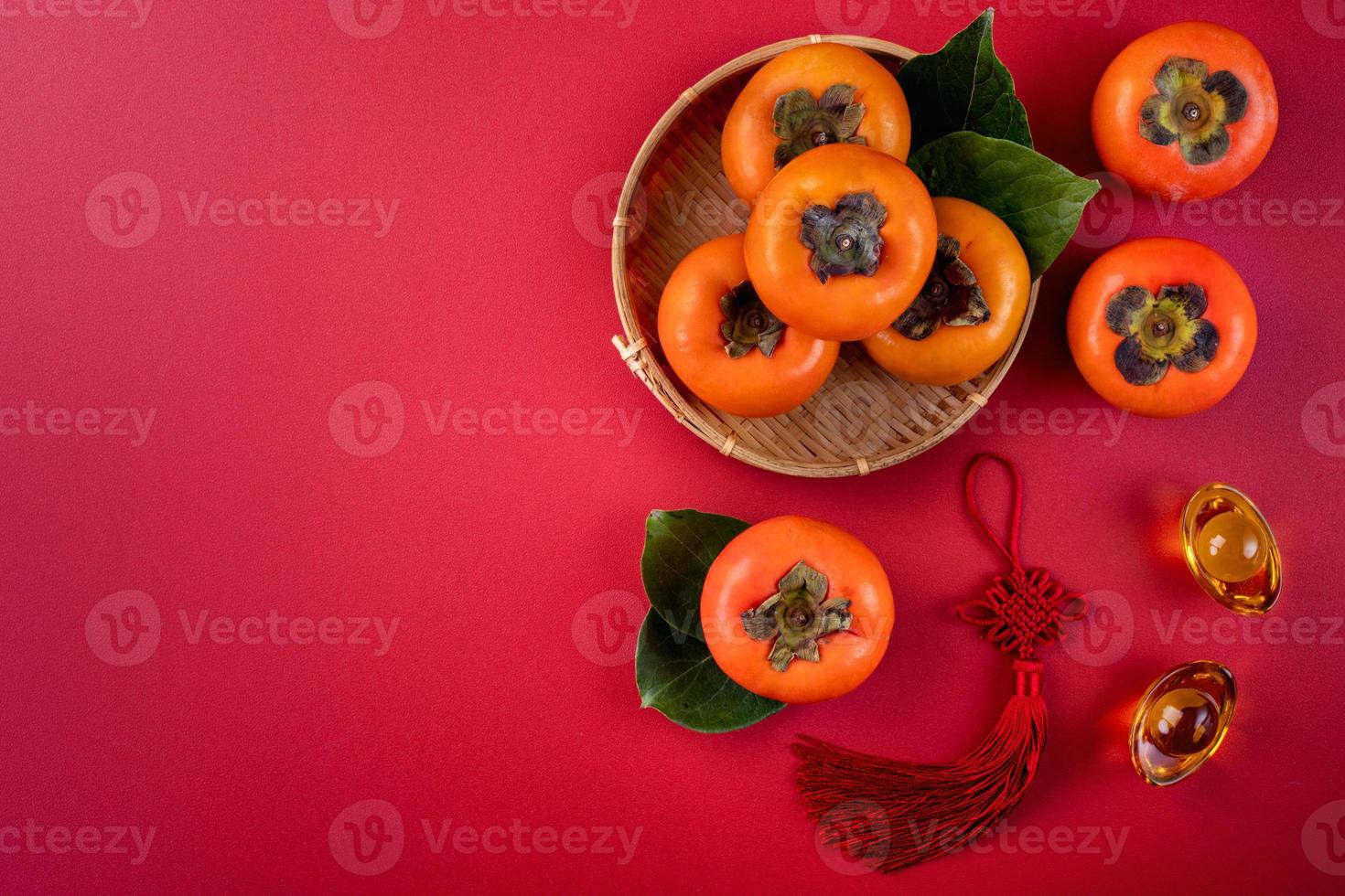 Draufsicht auf frische süße Persimonen mit Blättern auf rotem Tischhintergrund für das chinesische Neujahrsfest foto