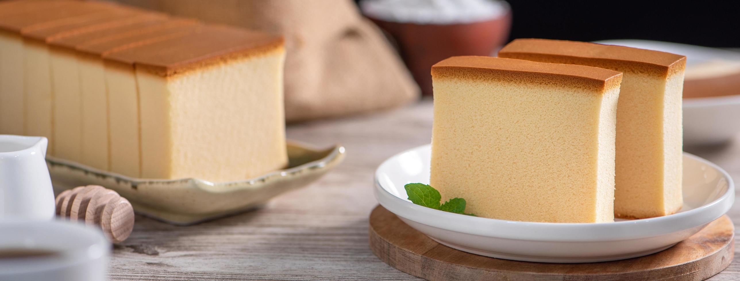 castella kasutera - köstliches japanisches geschnittenes schwammkuchenessen auf weißer platte über rustikalem holztisch, nahaufnahme, gesunde ernährung, kopierraumdesign. foto