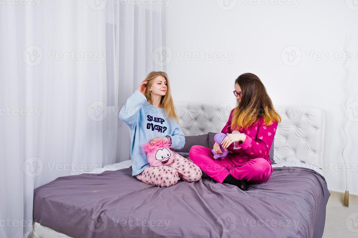 zwei befreundete mädchen im pyjama haben spaß auf dem bett im zimmer. foto