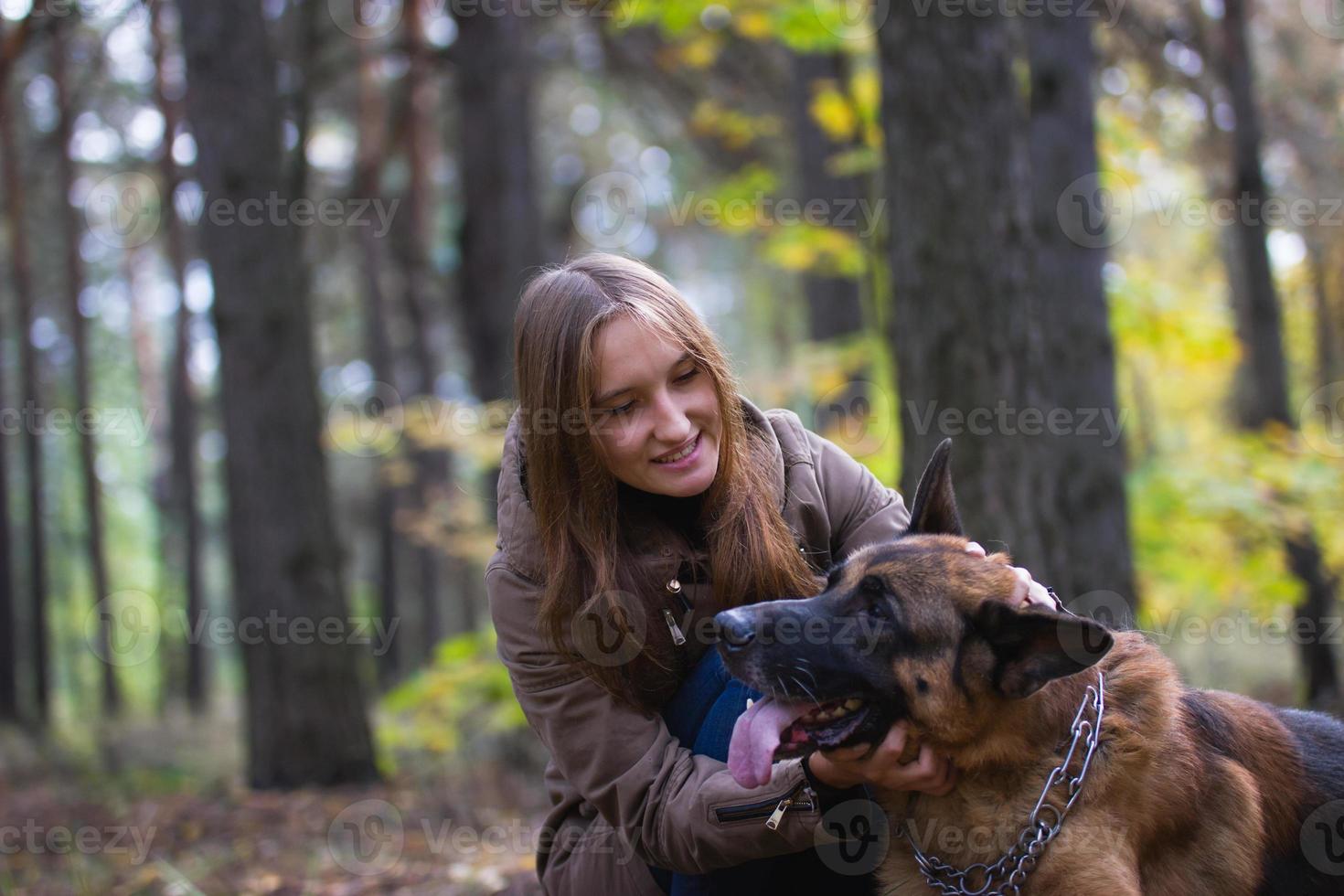 junges süßes lächelndes mädchen, das draußen im herbstwald mit deutschem schäferhund spielt foto