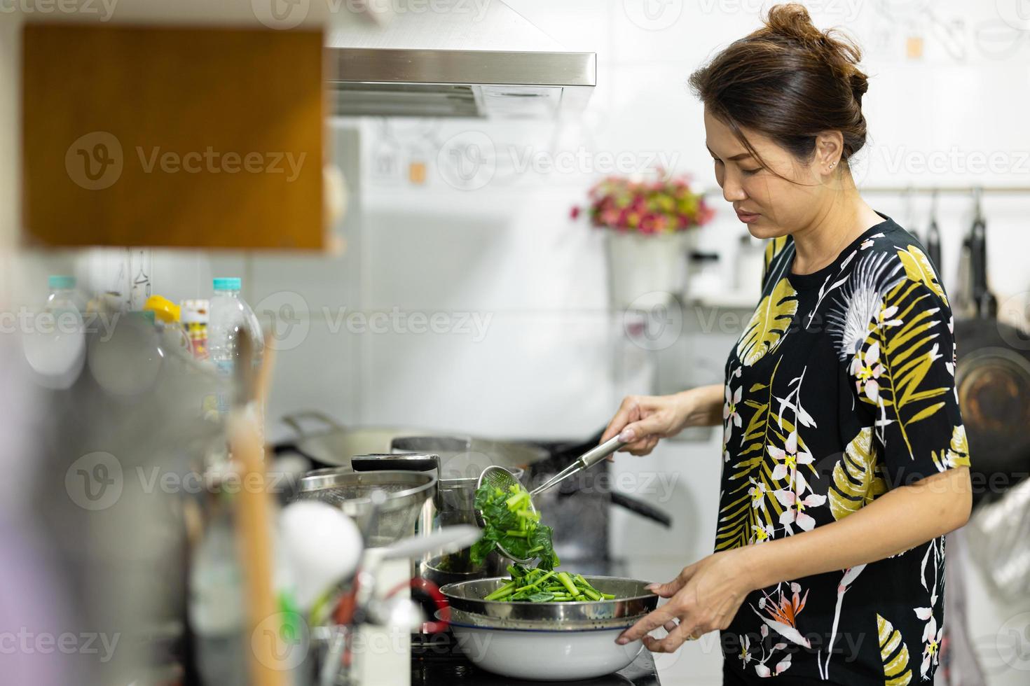eine authentische echte aufnahme einer asiatischen frau, die grünes gemüse für lebensmittel in der küche kocht und kocht. foto