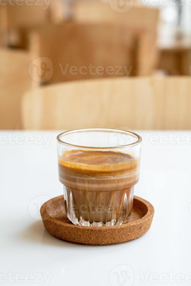 Schließen Sie ein Glas schmutzigen Kaffee auf einem Holztisch in einem Café-Shop. Kaffee mit Milch und Sahne. Getränke- und Getränkekonzept. foto
