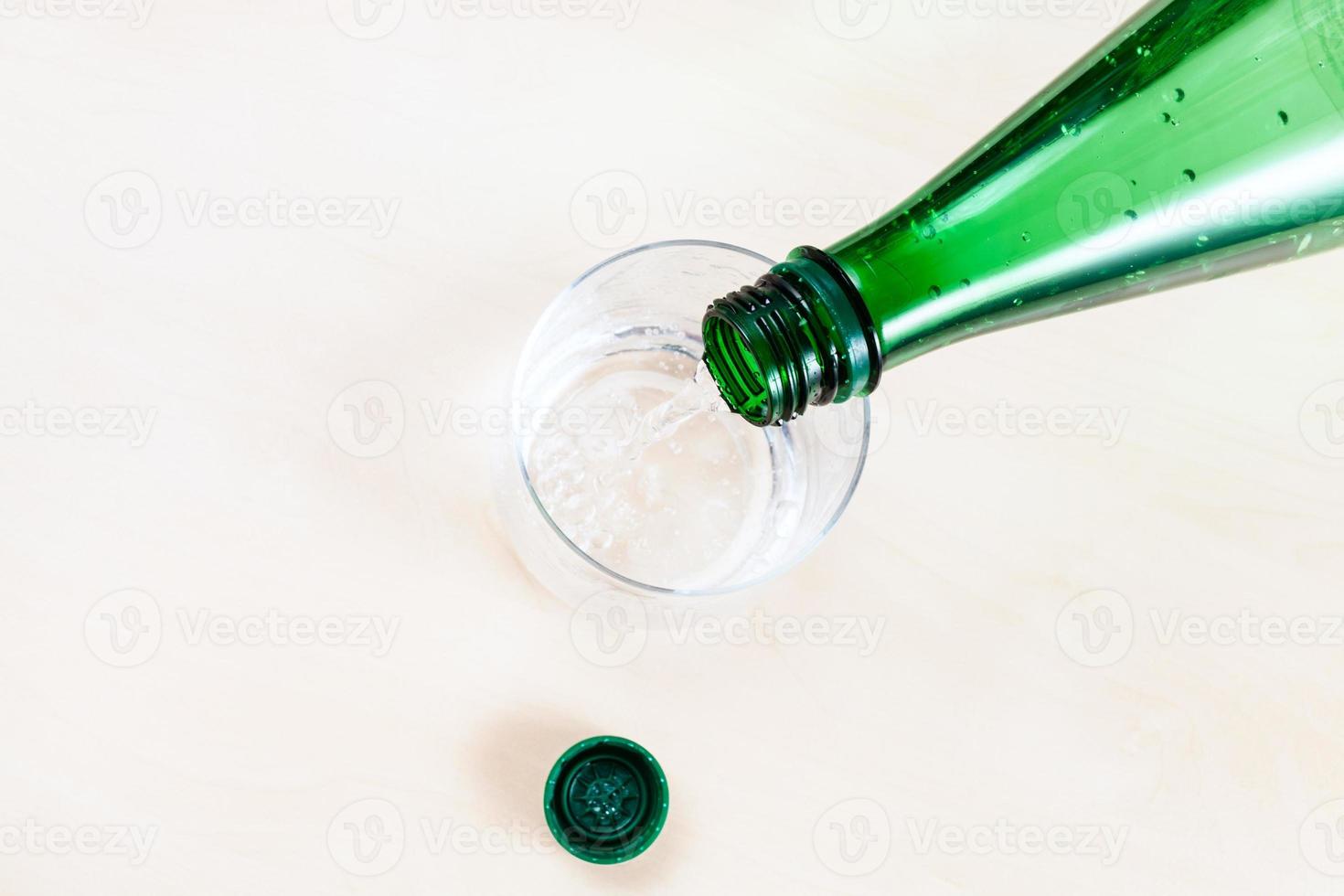 Wasser aus grüner Plastikflasche in Glas gießen foto