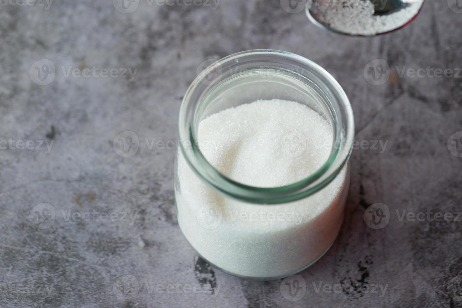 weißer Zucker und Löffel in einem Behälter auf schwarzem Hintergrund, foto