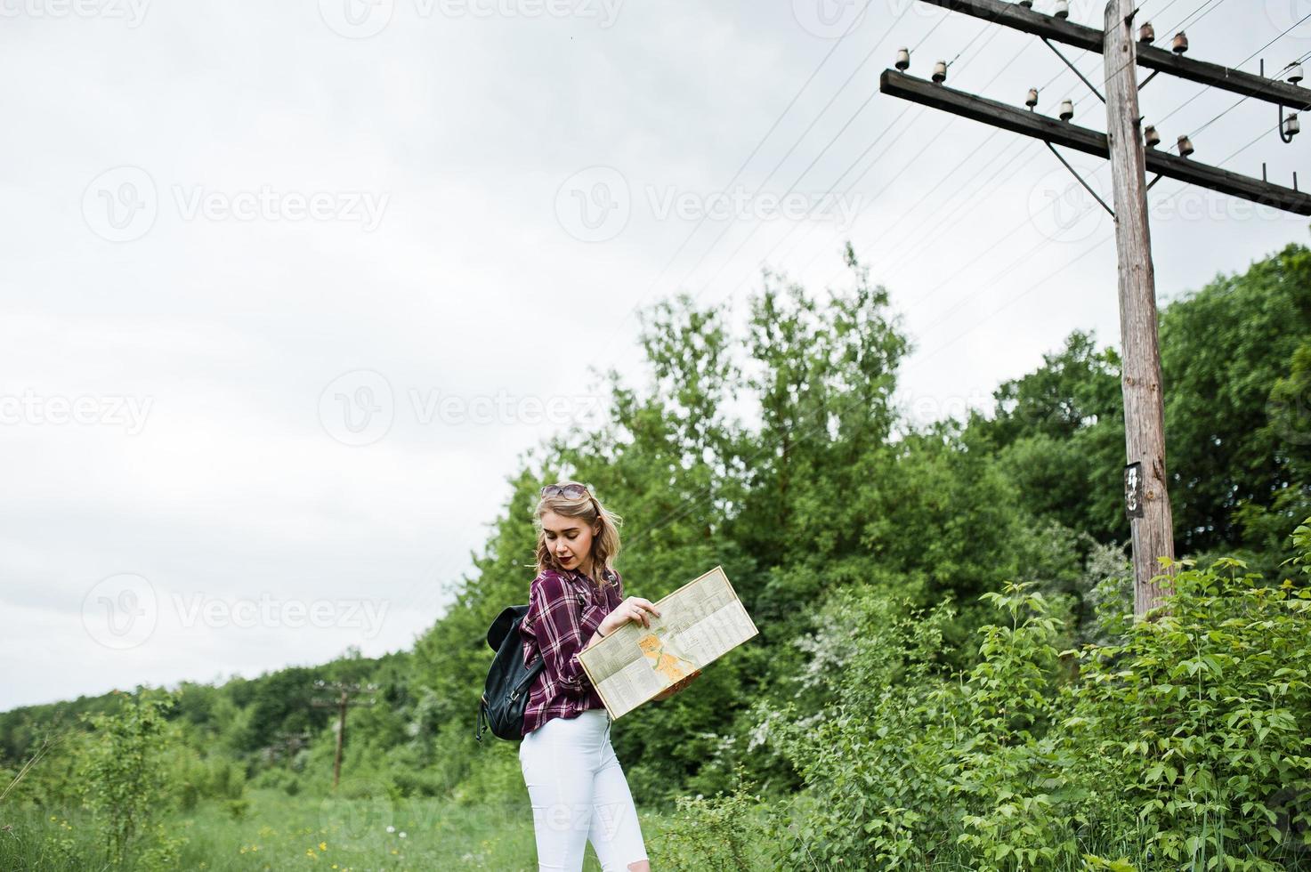 Porträt eines schönen blonden Mädchens im Tartanhemd, das mit einer Karte auf dem Land spazieren geht. foto