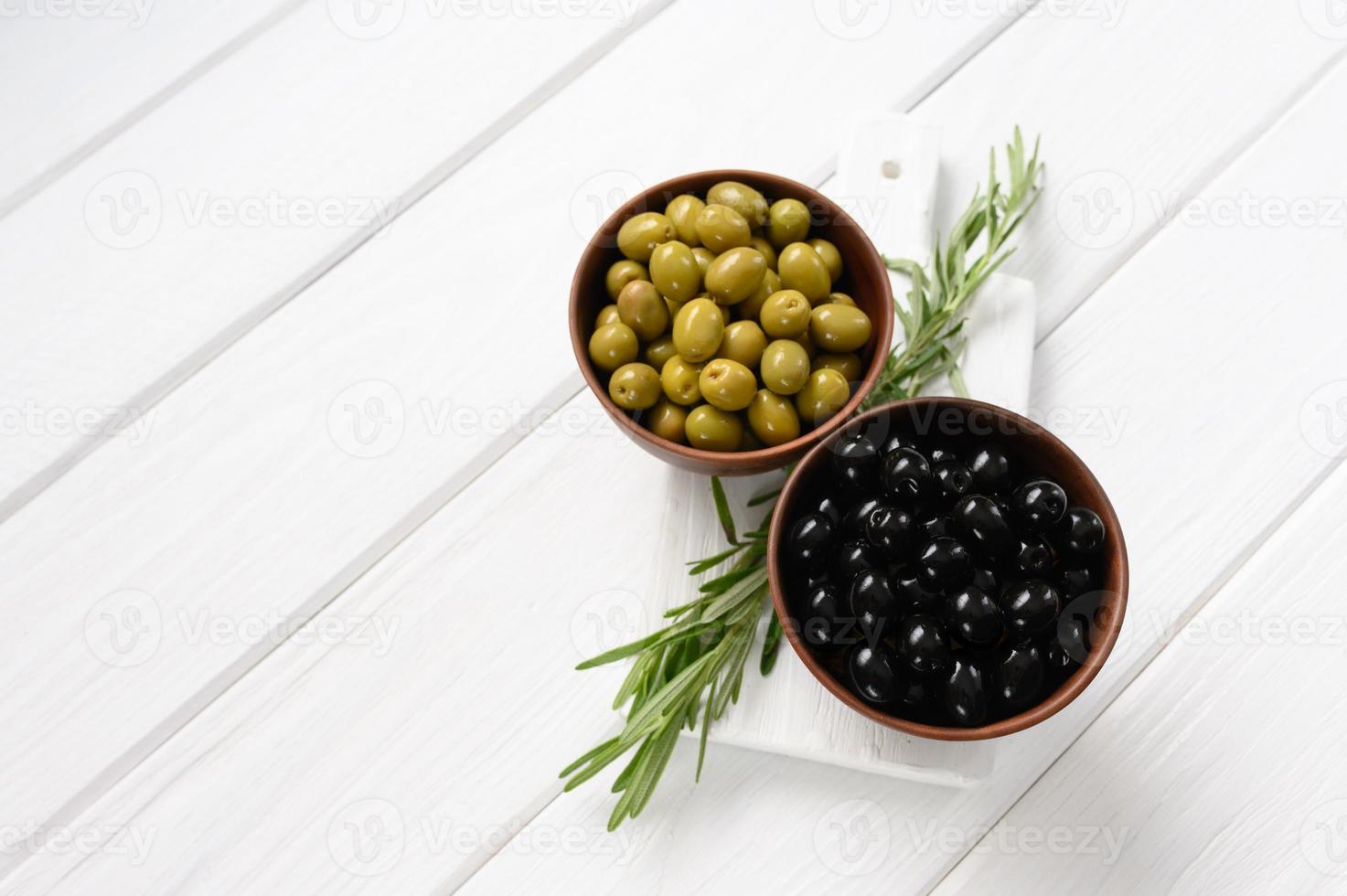 Schwarze und grüne Oliven auf weißem Holzhintergrund. foto