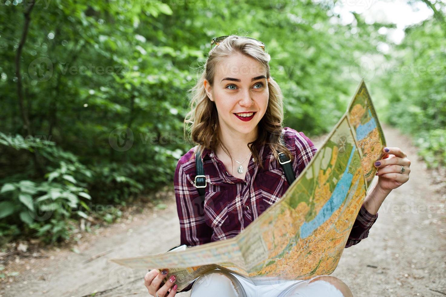 Porträt einer positiven jungen wunderschönen Blondine, die mit einer Karte in ihren Händen im Wald auf dem Boden sitzt. foto