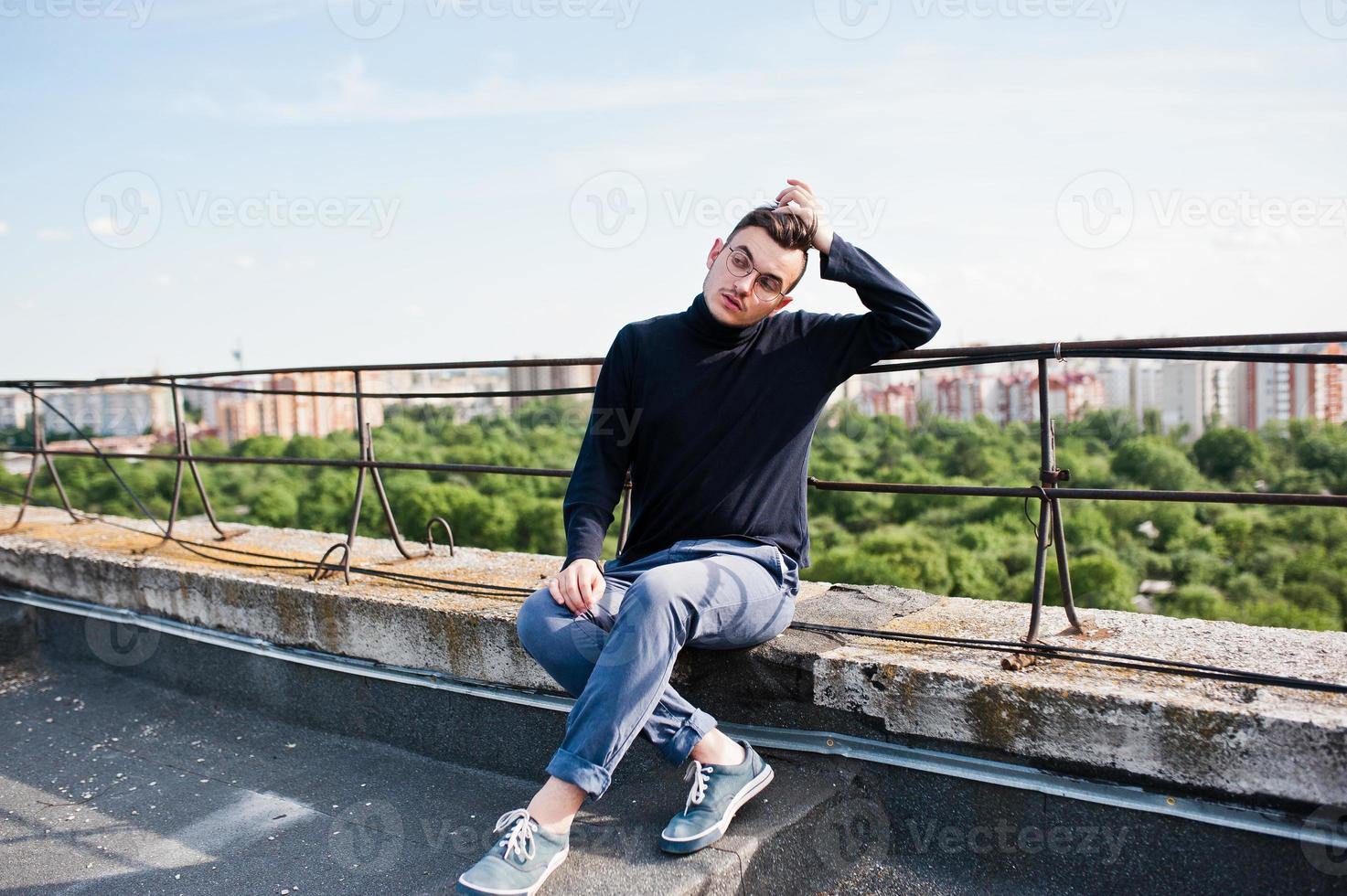 Träumer stylischer Macho in schwarzem Golf und Brille posiert auf dem Dach. foto
