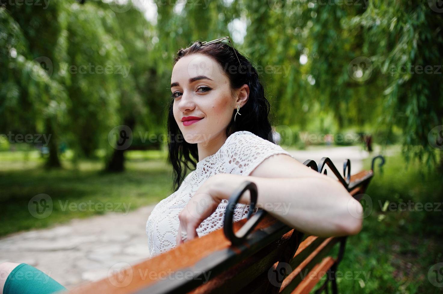 Brünettes Mädchen in grünem Rock und weißer Bluse posierte im Park und saß auf einer Bank. foto