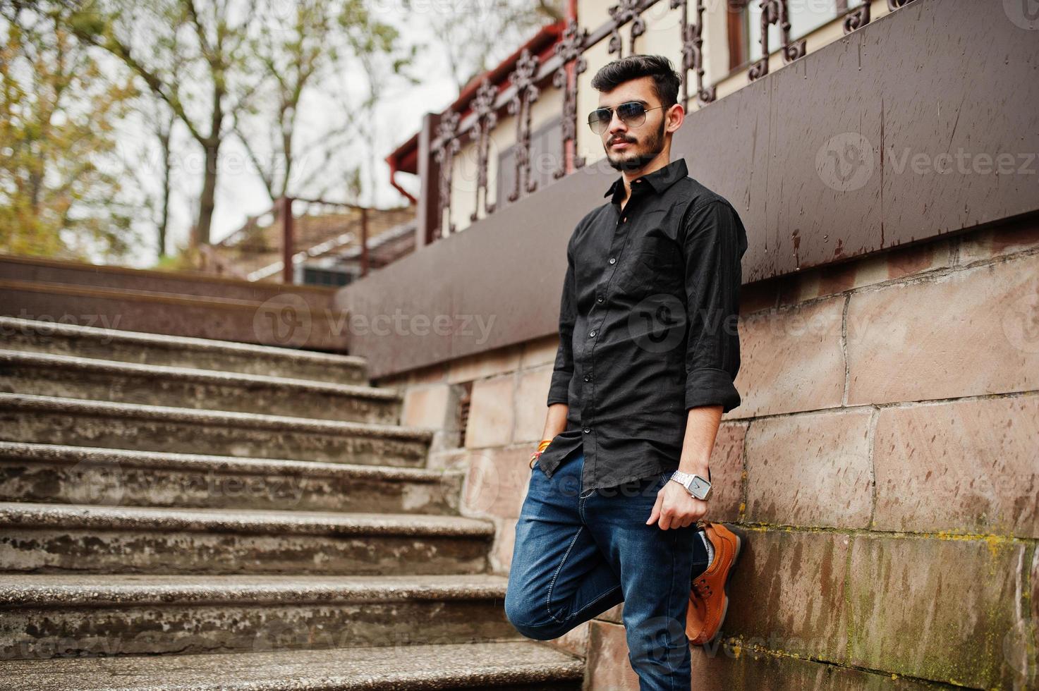 stilvoller indischer mann im schwarzen hemd und sonnenbrille posierte im freien. foto