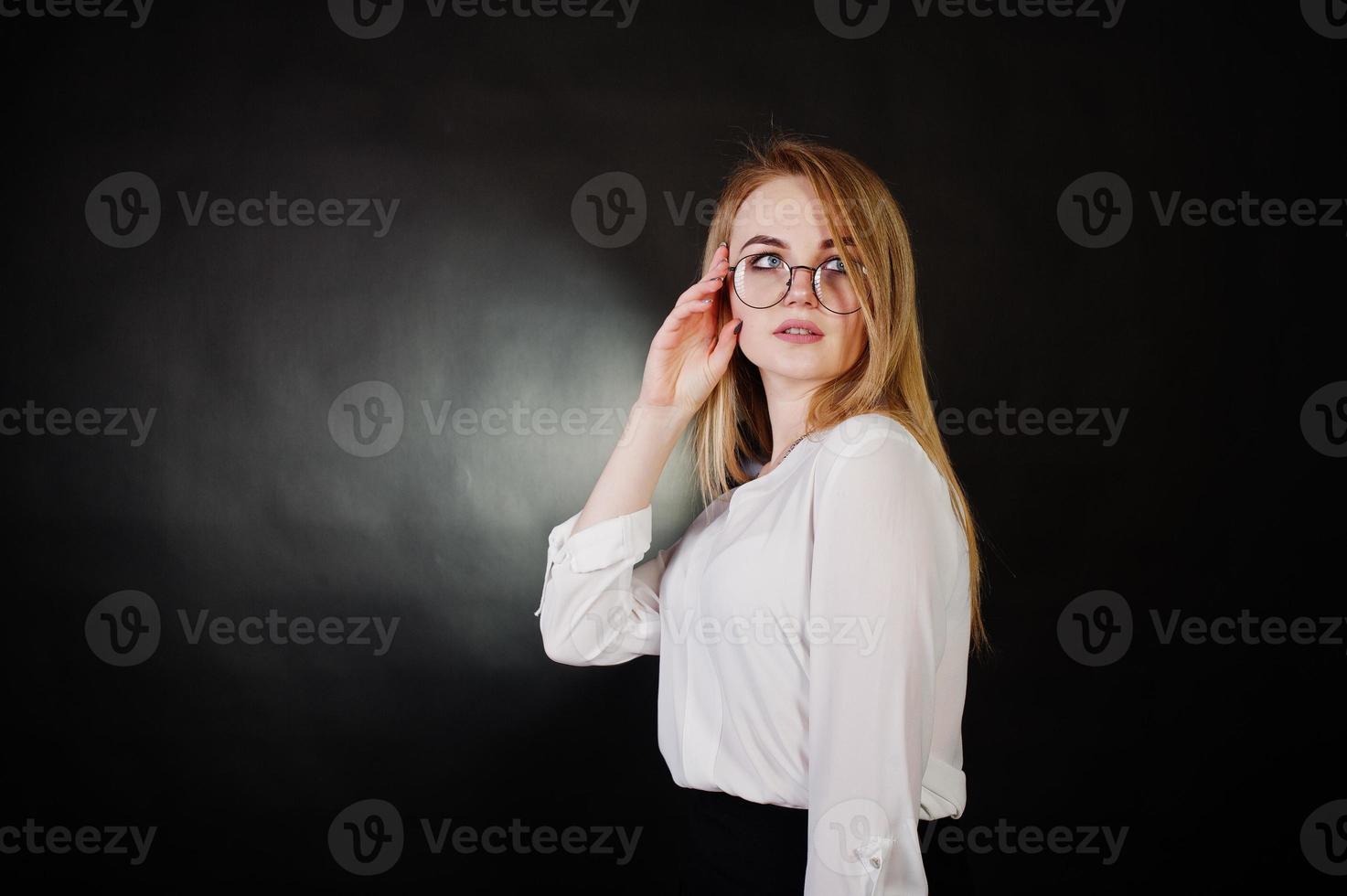 Studioporträt einer blonden Geschäftsfrau mit Brille, weißer Bluse und schwarzem Rock vor dunklem Hintergrund. erfolgreiche frau und stilvolles mädchenkonzept. foto