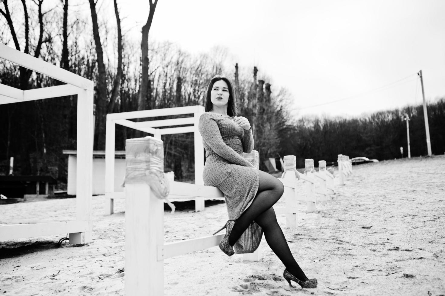 Porträt eines brünetten Mädchens in grauem Kleid, das an einer weißen Holzkonstruktion sitzt. foto